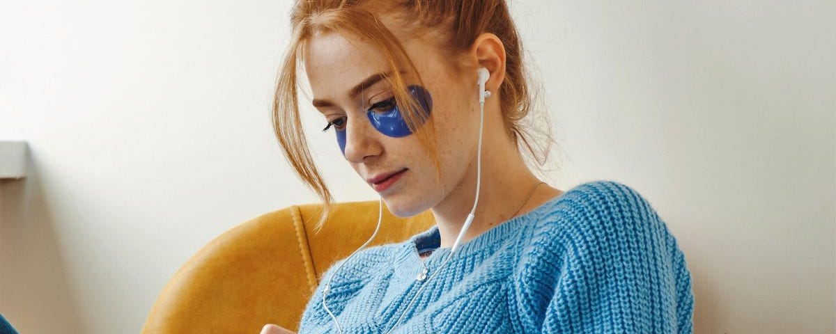 A young with red hair and a blue jumper woman is writing in a notepad.