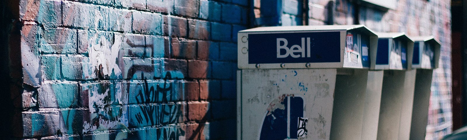 Three old Bell payphones mounted on a graffitied brick wall.