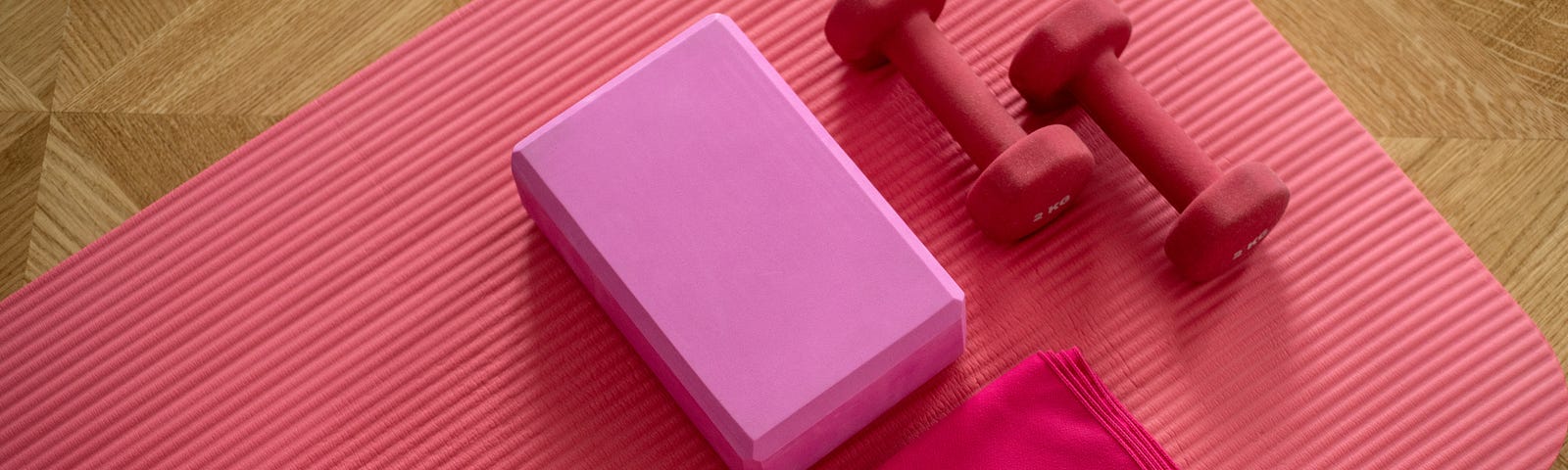 Pink yoga mat on parquet floor with pink block and pick towel