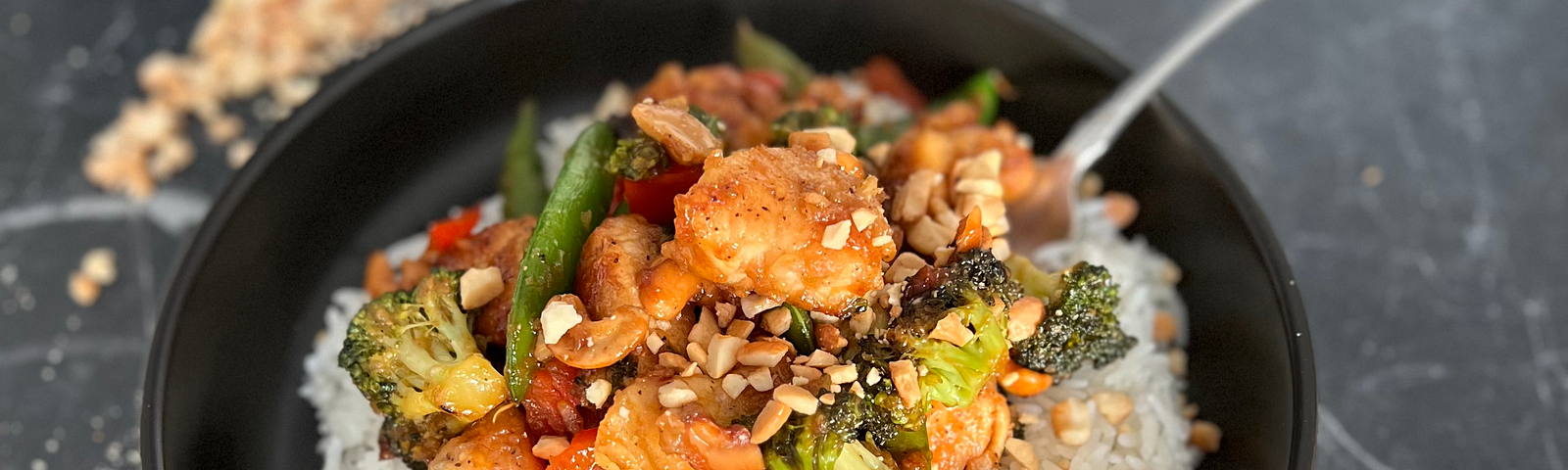 Cashew chicken stir fry on a marble surface with crushed peanuts