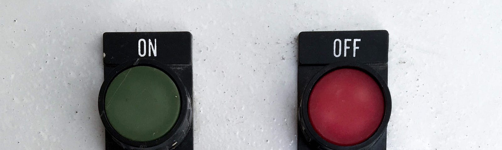 A dark green button marked ‘ON’ and a dark red button marked ‘OFF’ on a white wall. The ‘OFF’ button is pressed.