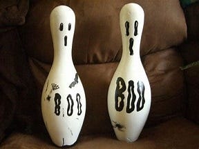 Two white bowling pins with ghost faces and the word Boo on them.