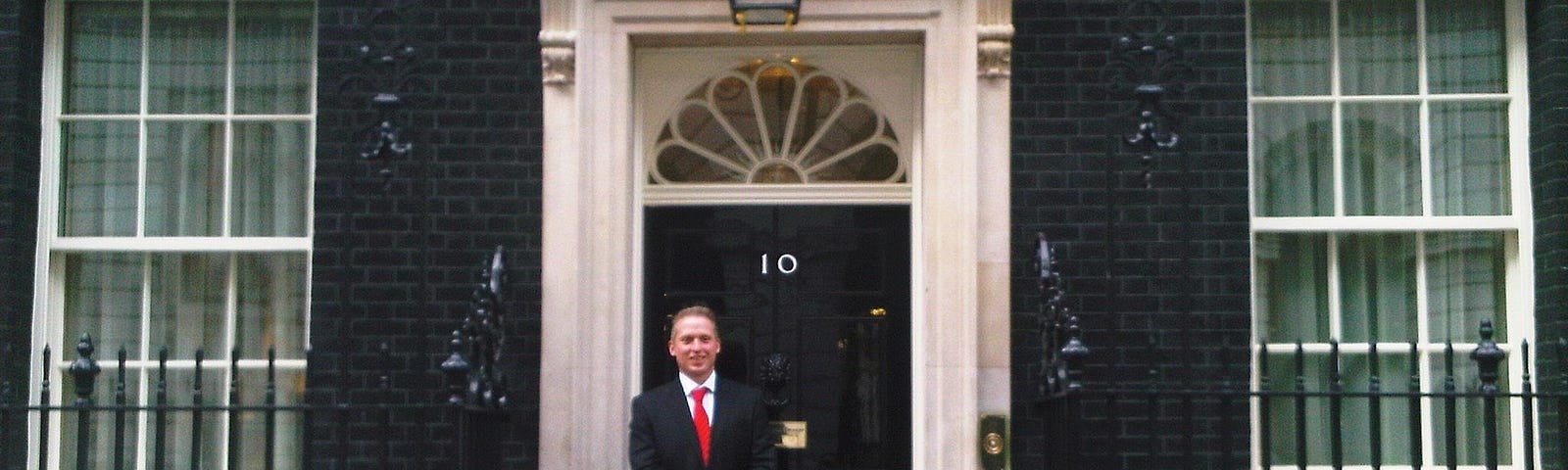 Neil Mapes, the author, dressed in a suit and tie outside the front door of number ten downing street.