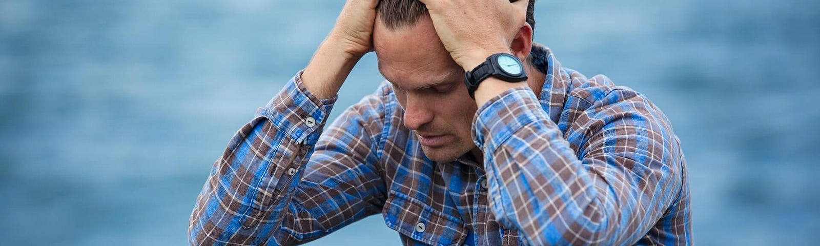 A lonely man is suffering from the dread of solitude and sitting by the sea with his hand holding his head out of the anxiety of being alone in the world.