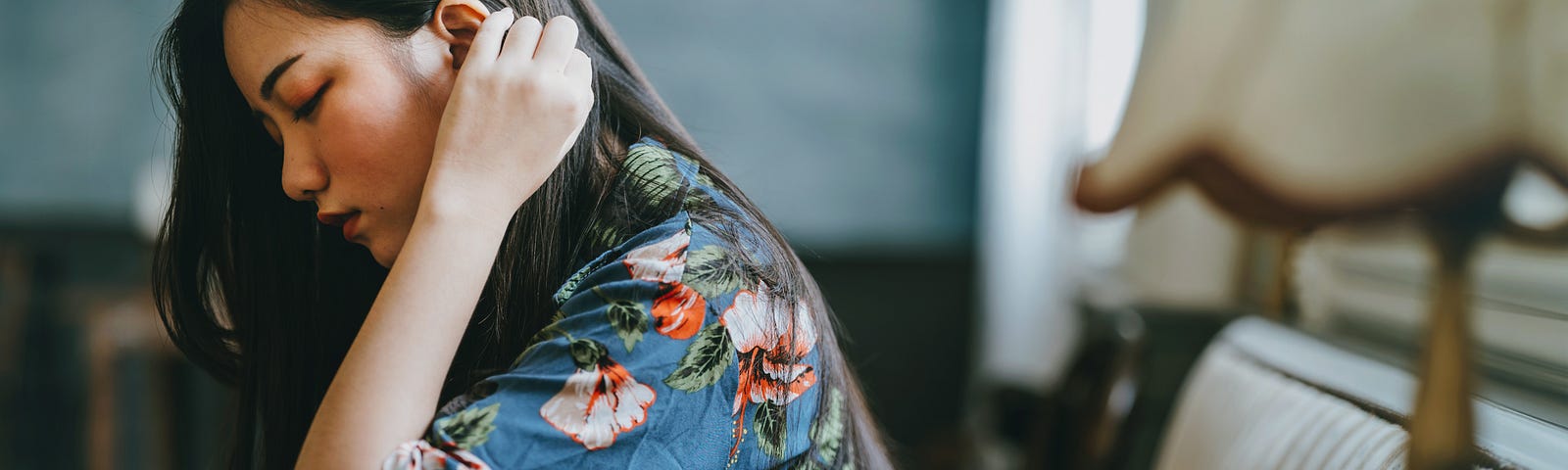 A pretty young woman stares pensively at the ground as she tucks her hair behind her ears.