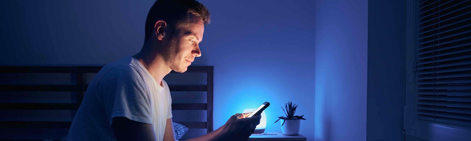 A man stares at his phone in the dark scrollign through a dating app.