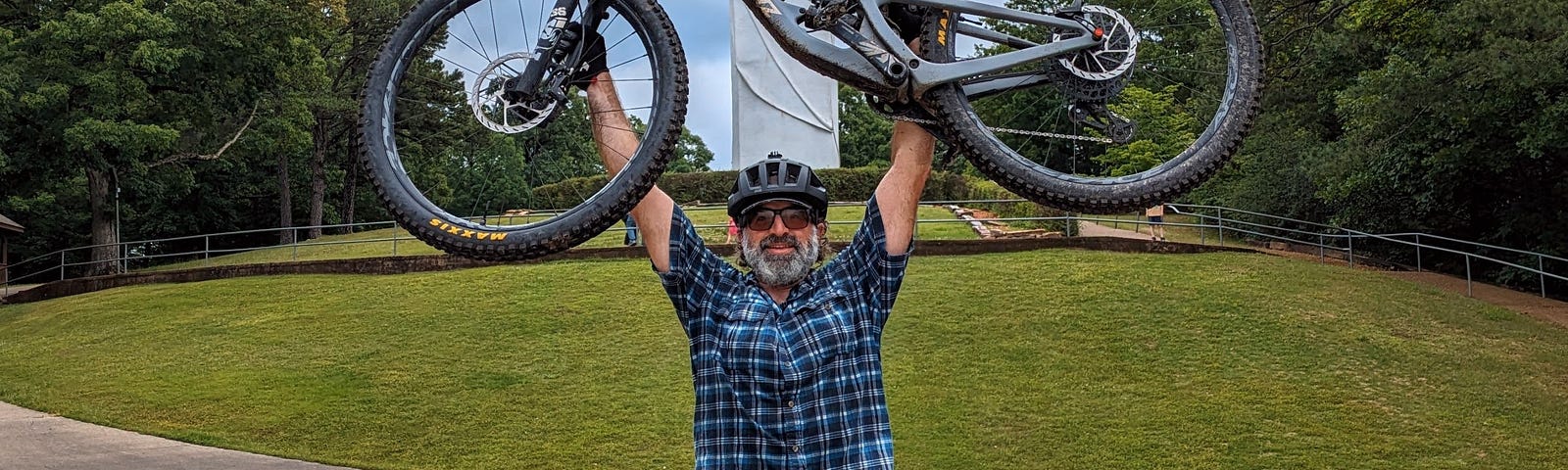 The author holding a mountain bike over his head, posed in front of the Christ of the Ozarks statue in Eureka Springs, Arkansas