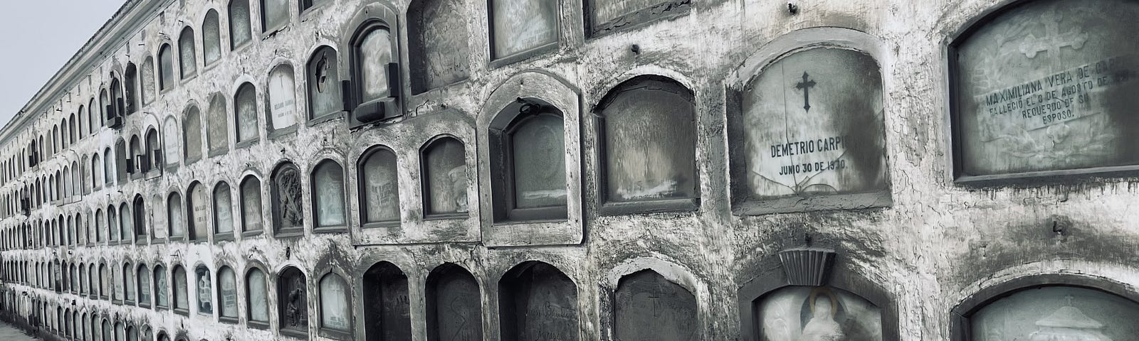 A gray wall lined with niches that hold tombs