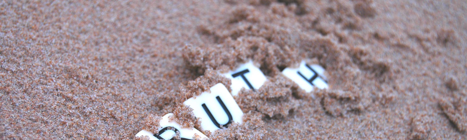 Tiles spelling “truth” partially buried in sand