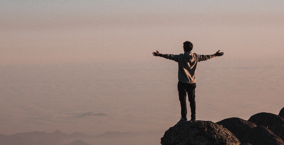 Man standing with arms spread out wide at edge of mountain