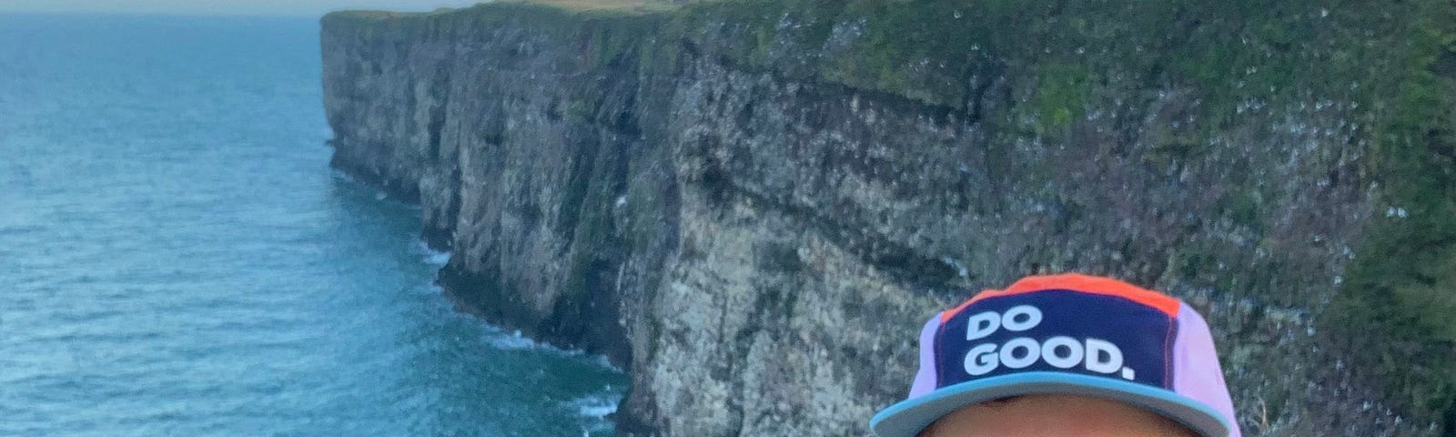 A hiker smiles happy with sea cliffs in the background.