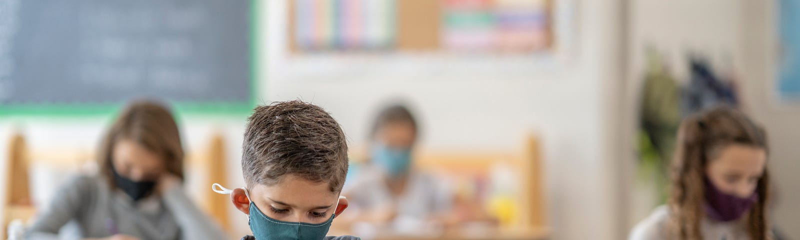 A student wearing a mask works at a school desk.