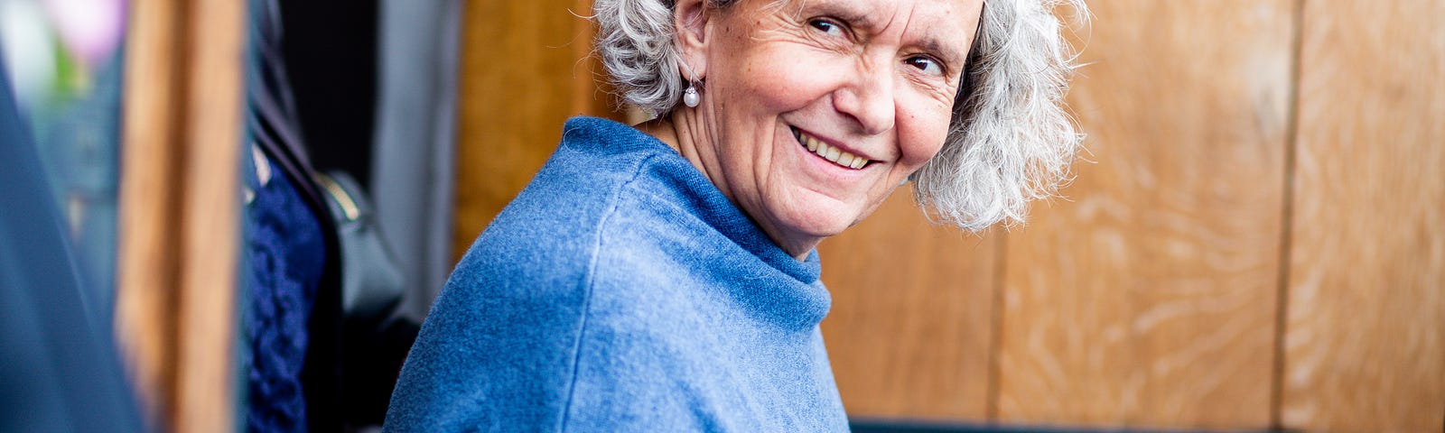 Beautiful gray haired older woman smiling at two men as she opens her door.