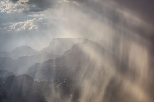 Image of rain storm over mountains, sunlit clouds in distance
