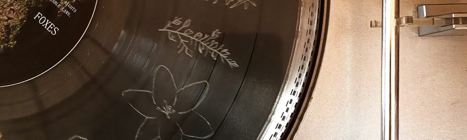 A section of a vinyl record on a silver turntable has outlines of flowers etched into the surface.