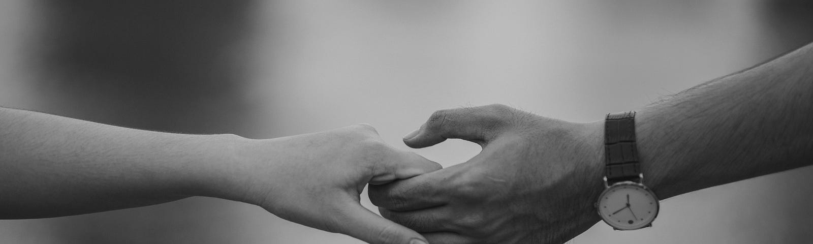 A close-up black and white photo of two people lightly holding hands
