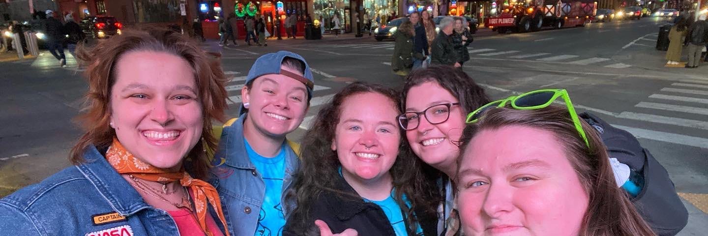 A group of five joyful queer friends smiling on a colorful street in Nashville.