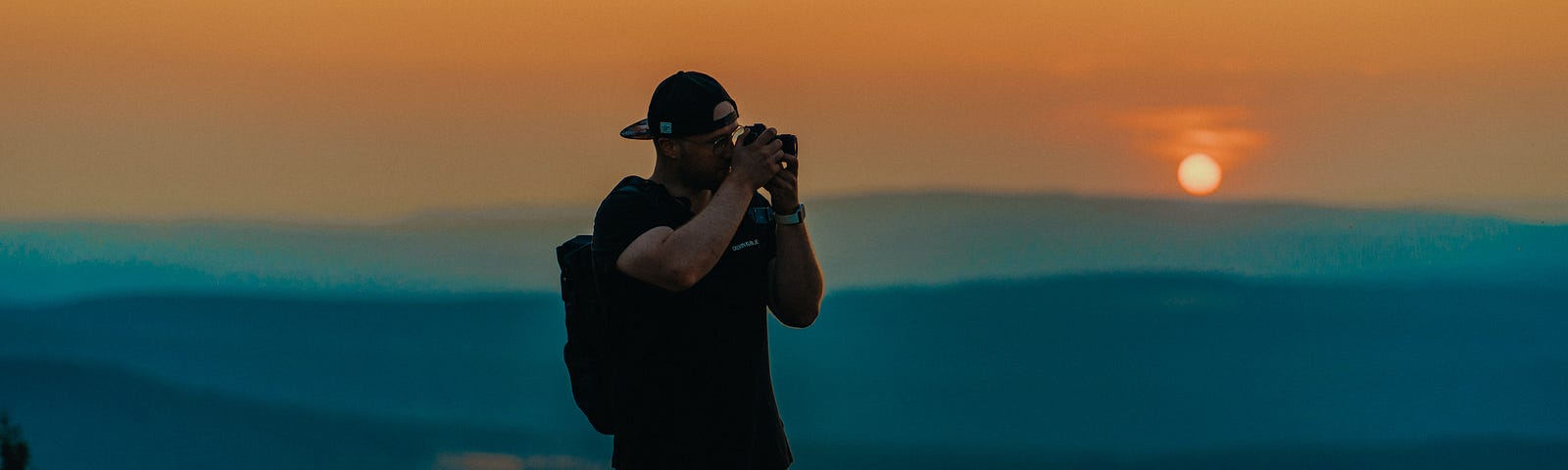 The sunset on the background. A man holds a camera to catch the moment.