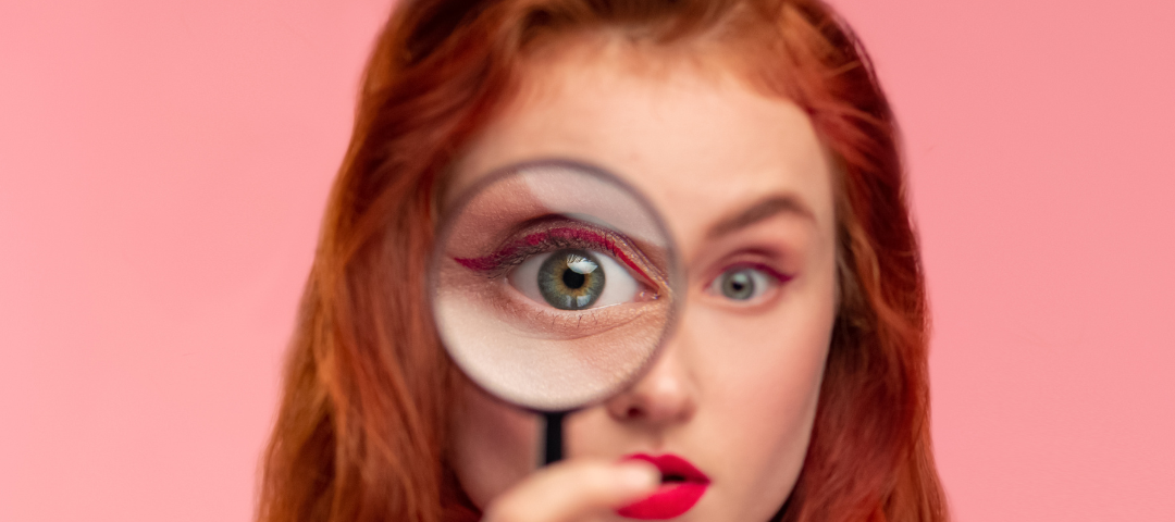 Red headed woman looks through a magnifying glass.
