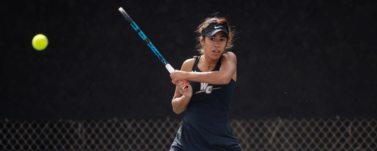 Action shot of a Whittier College Women’s Tennis player playing tennis. She is on the court with her blue racket and black Tennis ensamble.