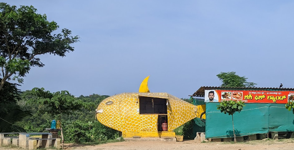 Photo of a yellow fish-shaped structure that serves as a makeshift roadside eatery. Had a board called Shashi Fish Land.