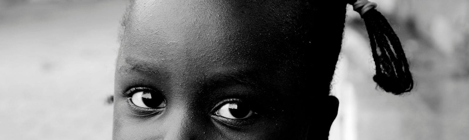 A black-and-white photo of a beautiful black girl looking into your eyes. This depicts how I’d sit my younger self down and share this story if I was told earlier.
