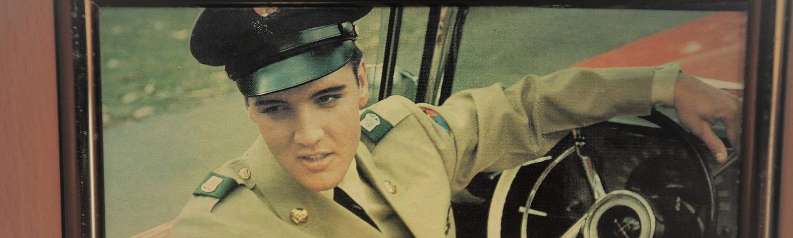 Framed photograph of Elvis Presley sitting in a car in his Army uniform.