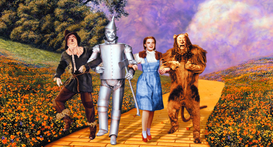The characters of the Wizard of Oz skipping down the yellow brick road. From L to R: Scarecrow, Tin Man, Dorothy, and the Lion.