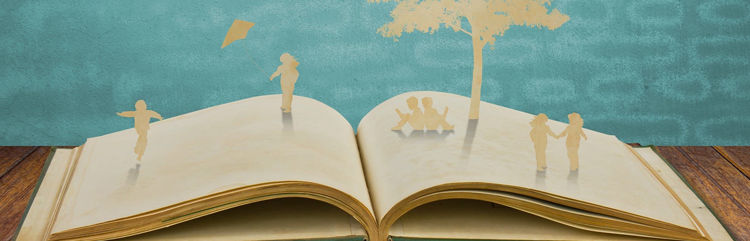 book opened on wooden table. emerging from book are beige silhouette of young children sitting reading a book under a tree