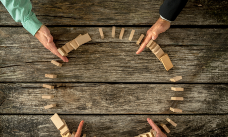 This image is of a circle of dominos with 4 hands reaching in to stop the dominos from falling.