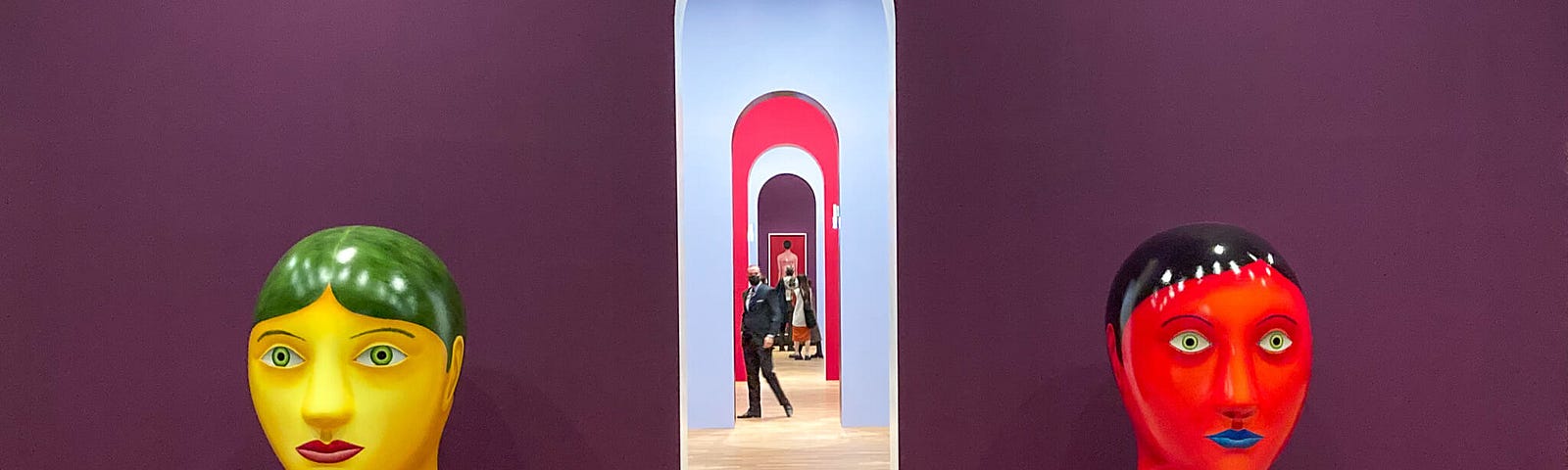 Art installation showing a large yellow head and a large red head on opposite sides of a narrow doorway in a purple painted wall