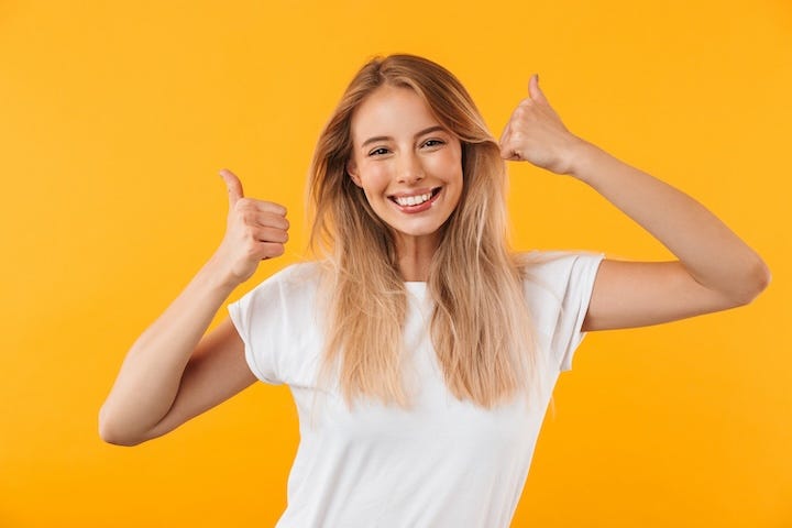 Portrait of a cheerful young blonde girl showing two thumbs up isolated over yellow background