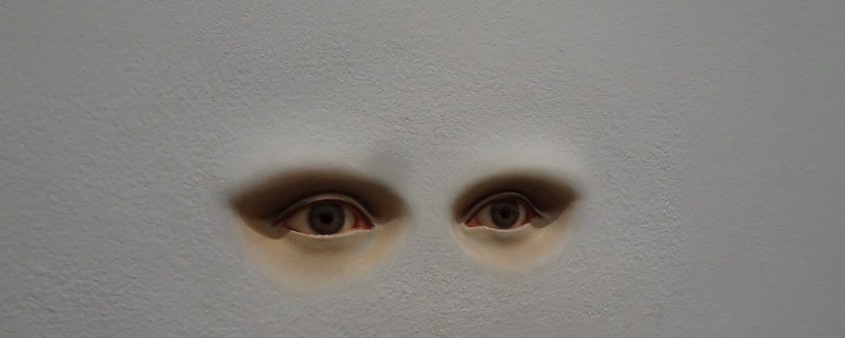 A pair of human eyes set into a blank, white wall.