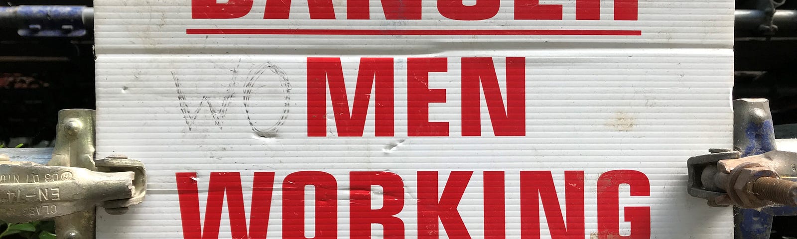 A ‘Danger: Men Working Overhead’ sign altered with pen to read ‘Danger: Women Working Overhead’.