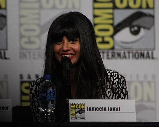 Jameela sits in front of a black and white background, smiling into mic, wearing black and white blouse