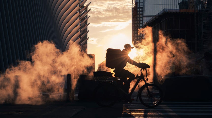 Silhouette of man cycling through steam on New York street during sunrise