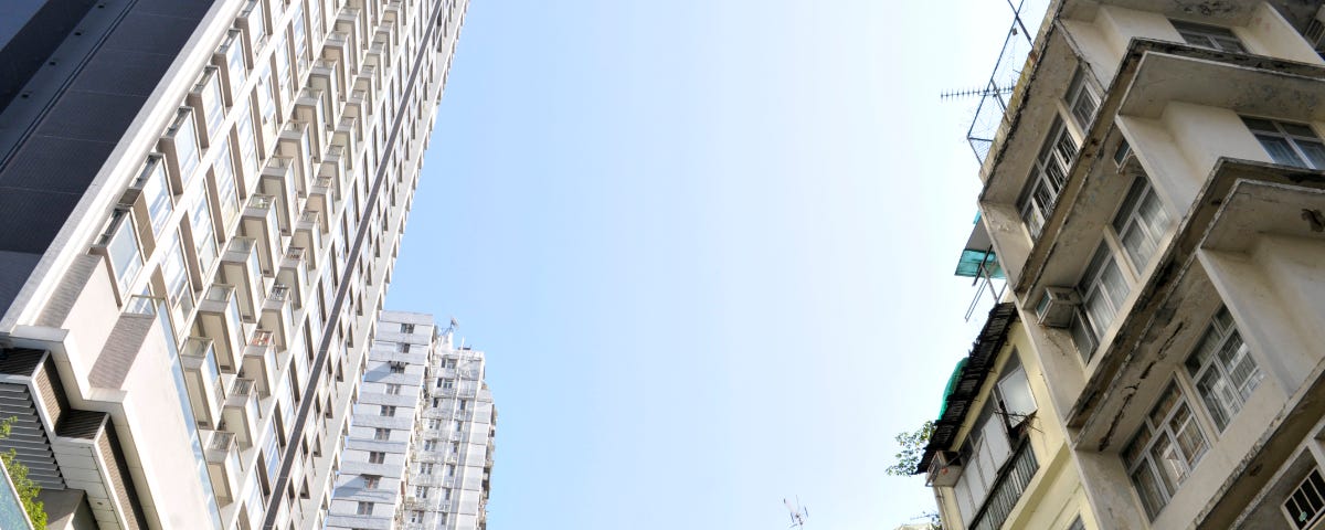 View from below to the blue sky, high rise on the left, tong lau on the right.