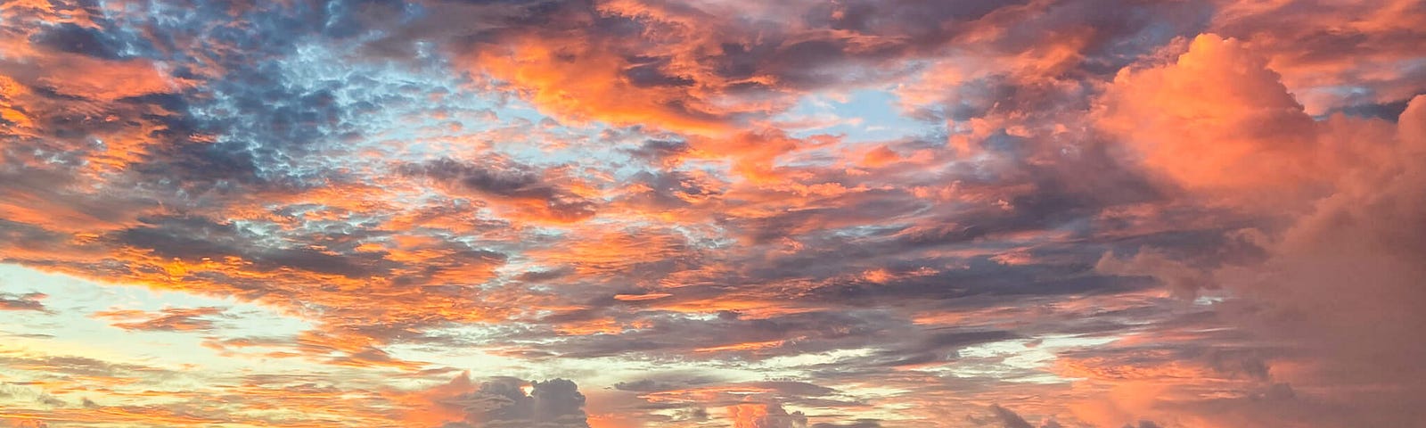 Orange and pink colored clouds in a big sky over an ocean seen from the beach