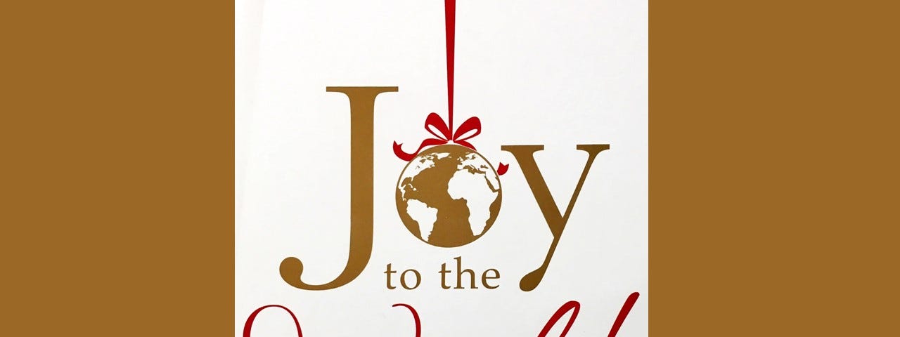 The stylized words, Joy to the World, with the ‘o’ in Joy rendered as a hanging globe of the world on cream-gold background.