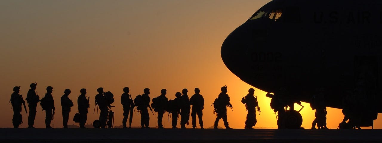 Soldiers waiting in line to board a plane at sunset