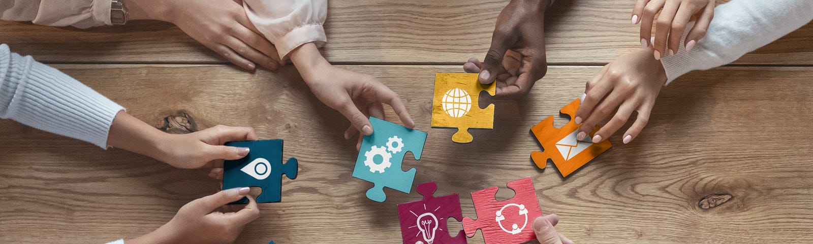 The hands of six people hold differently-coloured jigsaw pieces, representing the building of a complete interdisciplinary picture with different disciplinary elements