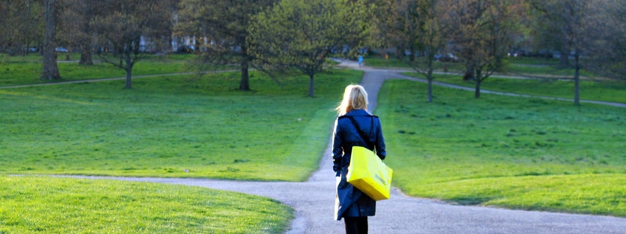 A woman walking through a park, approaching a crossroad of paths.