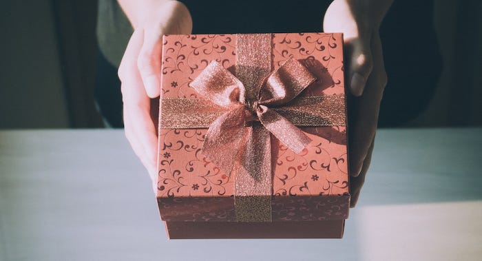 A woman’s hands holding out a gift box with a large bow.