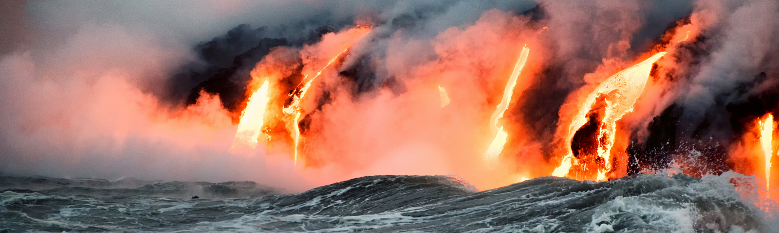 The image shows a dramatic scene of molten lava pouring into the ocean, creating plumes of steam as the intense heat meets the turbulent waves. The bright orange glow of the lava contrasts with the dark, stormy waters, highlighting the powerful interaction between volcanic activity and the sea.