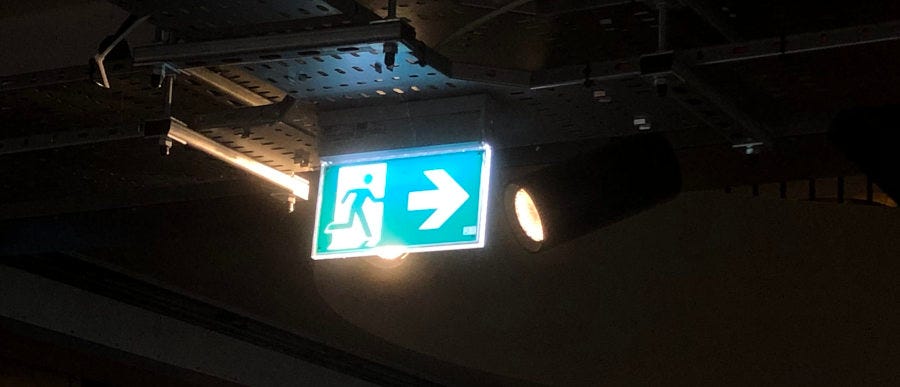 Emergency Exit sign: Green man symbol on white door with white arrow indicating direction of exit.