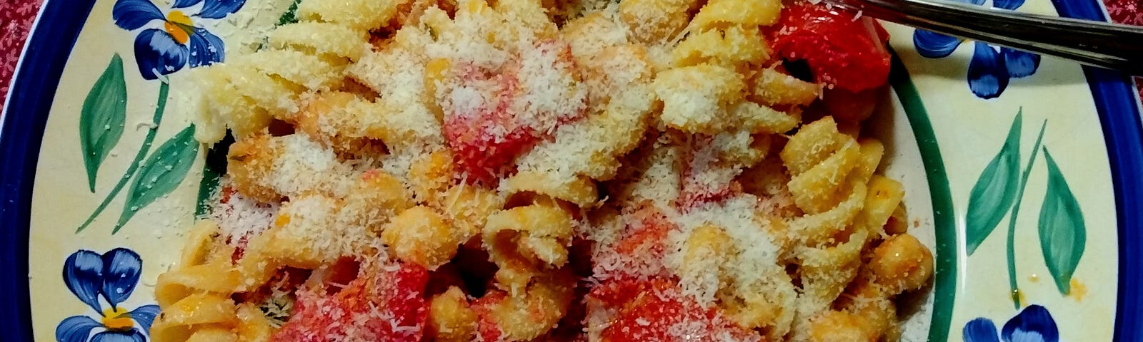 Photo of Thunder and Lightning dish served in a bowl. There is rotelli pasta, tomatoes, and ceci beans in this dish. There is freshly grated Romano cheese on top.