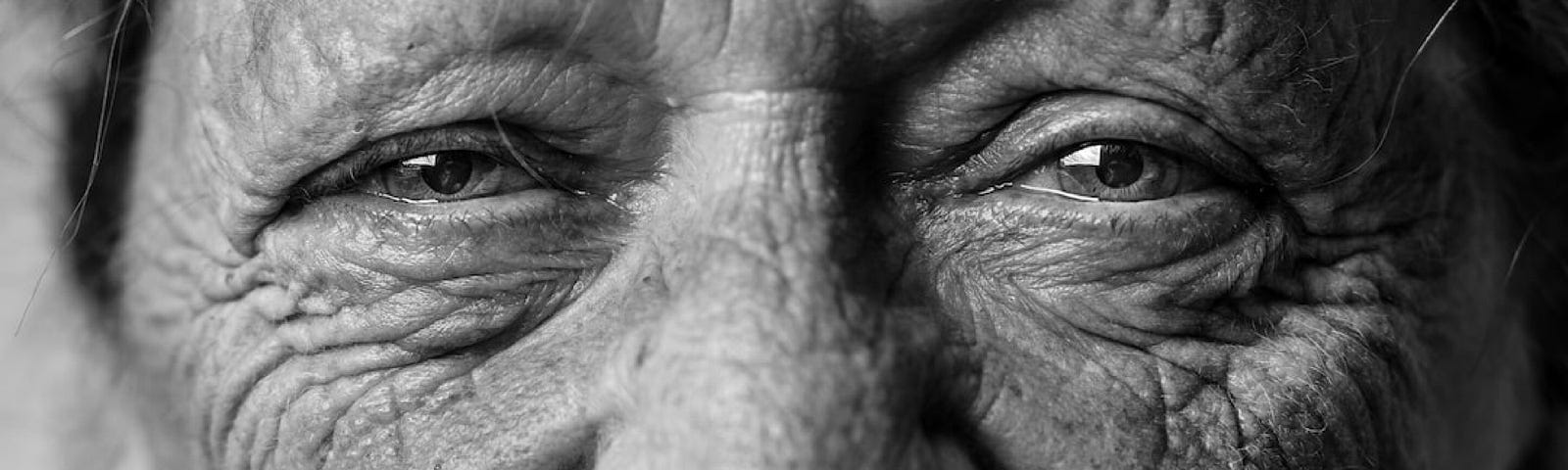 A black and white photo of an elderly woman with a very lined and wrinkled face smiles sweetly into the camera.