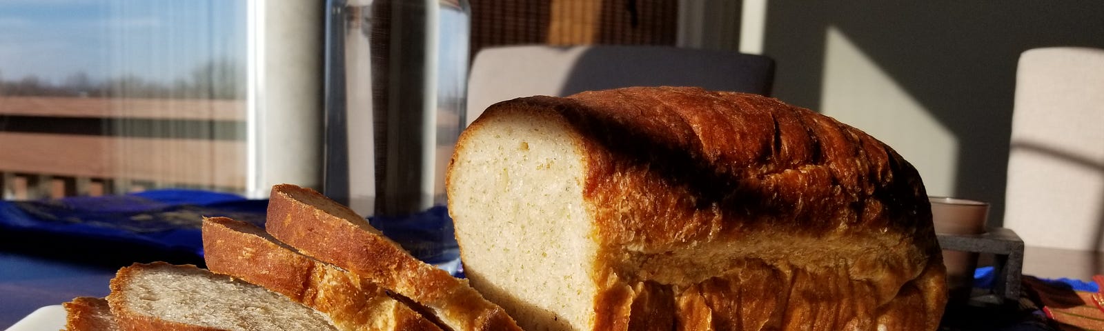 A sunlit loaf of bread with four slices exposing the deliciously open crumb