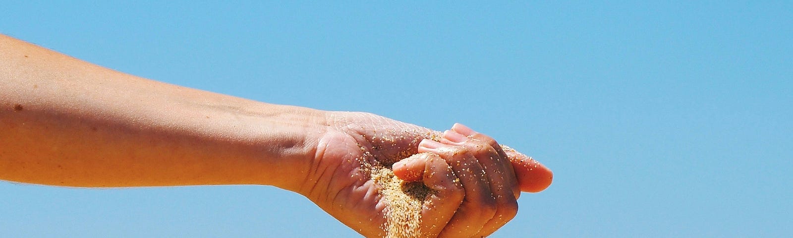 Person’s hand holding sand at the beach.