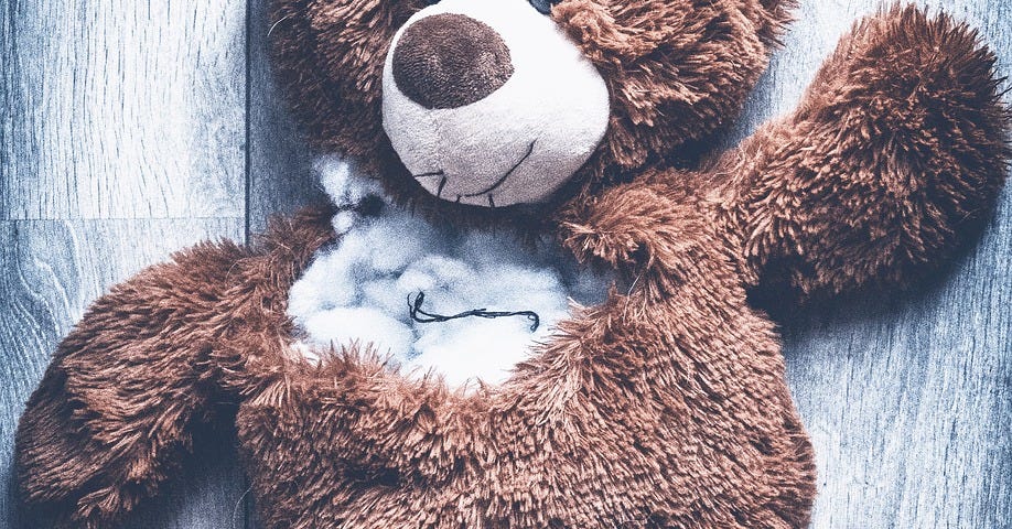 A teddy bear that has been torn apart and has stuffing exposed from large rips and tears.